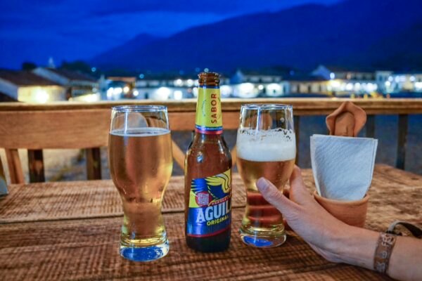 Two glasses of beer and a bottle of Águila on a wooden table, with twinkling lights of Villa de Leyva in the background.