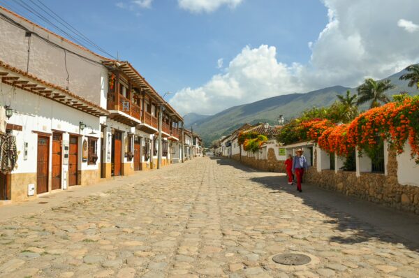Colonial street in Villa de Leyva lined with whitewashed buildings, cobblestones, colorful flowers, and mountain views