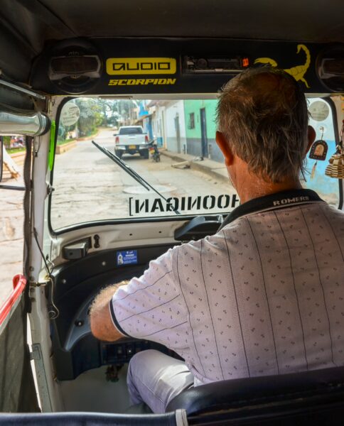 View from inside a tuk-tuk in Villanueva, Santander, Colombia, showcasing a driver on a vibrant street lined with colorful buildings.