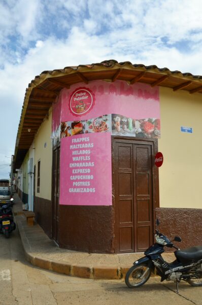 Pink-walled café in Villanueva, Santander, showcases vibrant signage and wooden details, inviting passersby to explore.