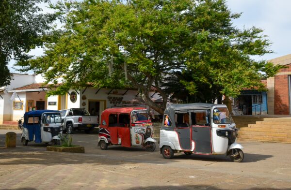 Tuk-tuks parked in Villanueva’s main square under a large tree, with colonial-style buildings in the background