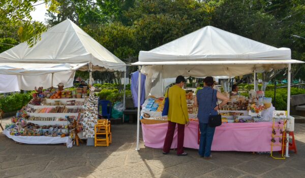 Colorful market stalls in Villanueva, Santander, display handmade crafts under white tents, surrounded by lush greenery.