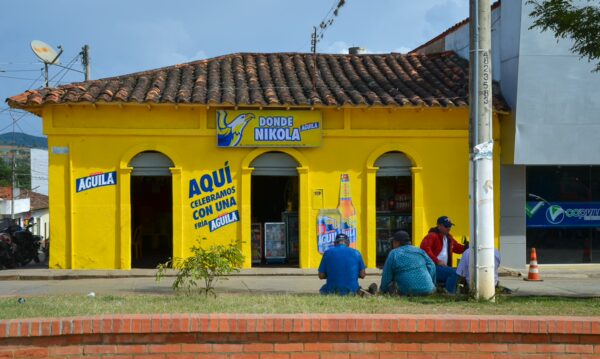 Bright yellow storefront in Villanueva, Santander, with a rustic roof, featuring local signage and two people sitting nearby.