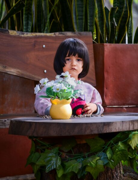 Young child seated at an outdoor table with a small vase of white flowers in Villanueva, Santander