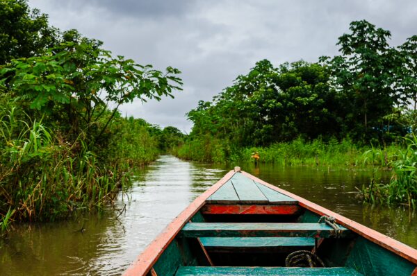 Quiet boat navigating through lush greenery in Gamboa Nature Reserve, Loreto, Peru, under a cloudy sky.