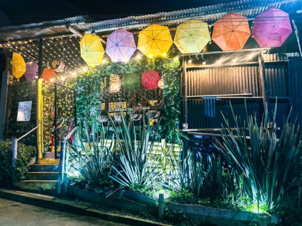 Colorful umbrellas hang above a vibrant café adorned with plants and lights, located in Salento, Quindío, Colombia.
