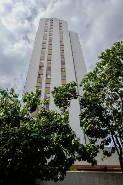 Towering white building against a cloudy sky, surrounded by lush green foliage in Medellín, Antioquia, Colombia.