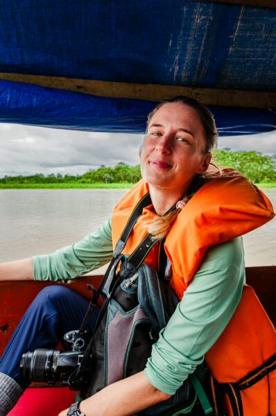 Smiling traveler in an orange life jacket sits in a boat on the water, surrounded by lush greenery in Gamboa Nature Reserve, Loreto, Peru.