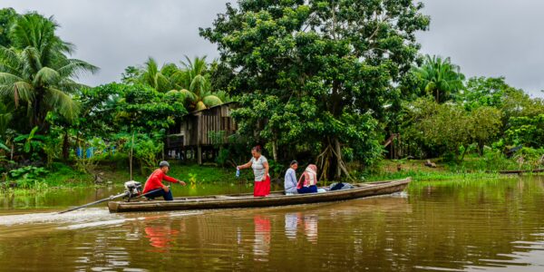 Local fishermen navigate the calm waters of Gamboa Nature Reserve in Loreto, Peru, surrounded by lush greenery.
