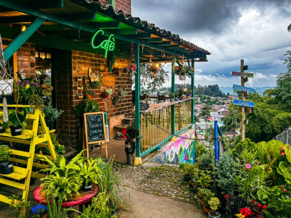 Vibrant café with neon sign, colorful plants, and scenic views in Alto de la Cruz, Salento, Quindío, Colombia.