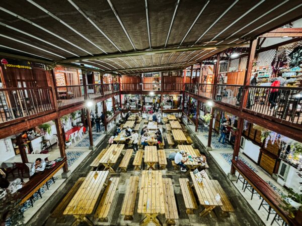 Vibrant recinto gastronómico in Salento features wooden tables and bustling diners under a spacious, rustic interior.