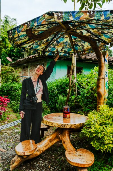 Vibrant wooden table and umbrella in a garden setting with a woman posing joyfully in Velez Salento, Quindio, Colombia.