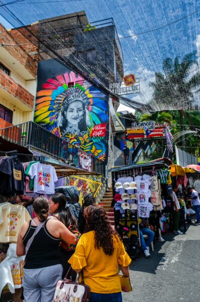 Vibrant street scene in Comuna 13, Medellín, displaying colorful murals and bustling market stalls filled with local crafts.