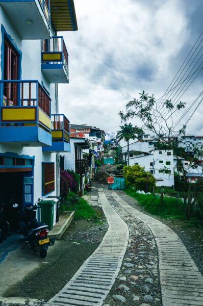 Charming cobblestone path lined with colorful buildings in Salento, Quindío, Colombia, under a cloudy sky.