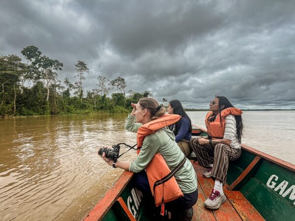 Explorers in life jackets on a boat at Gamboa Nature Reserve, surrounded by lush greenery and a cloudy sky in Loreto, Peru.
