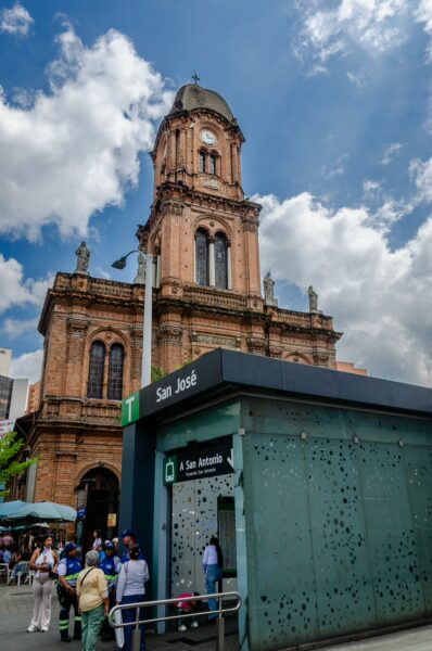 San José Church towers above a bustling Medellín street, with vibrant blue skies and white clouds in the background.