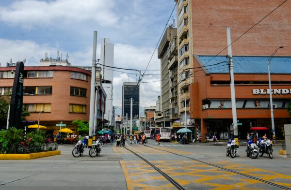 Bustling street scene in Medellín, Antioquia, featuring colorful buildings, shops, and motorcycles among pedestrians.