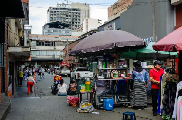 Busy street scene in Medellín, Colombia, featuring market stalls, colorful umbrellas, and vendors selling various goods.