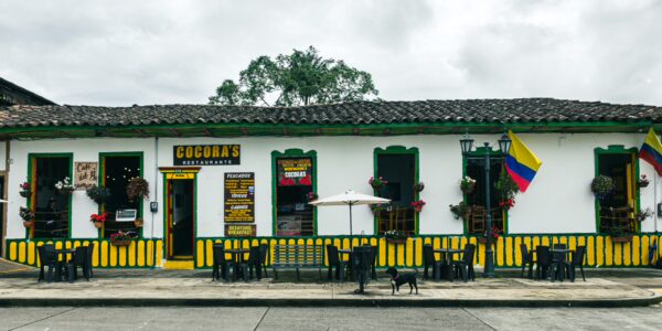 Colorful colonial buildings with yellow accent stripes house shops in Plaza Bolivar, Salento, Quindio, Colombia. A dog rests nearby.