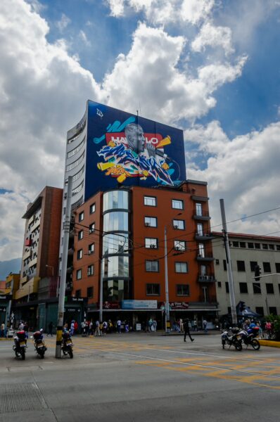 Vibrant street scene in Medellín, featuring colorful murals on buildings and busy traffic under a cloudy sky.
