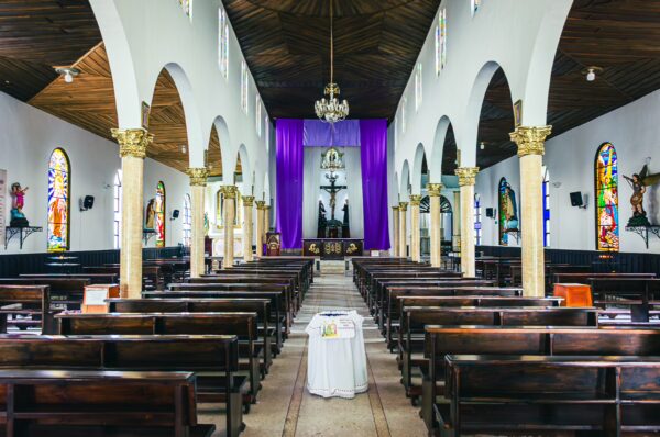 Inside Nuestra Señora de Carmen in Salento, Quindío, colorful stained glass windows contrast with wooden pews and a purple drape.