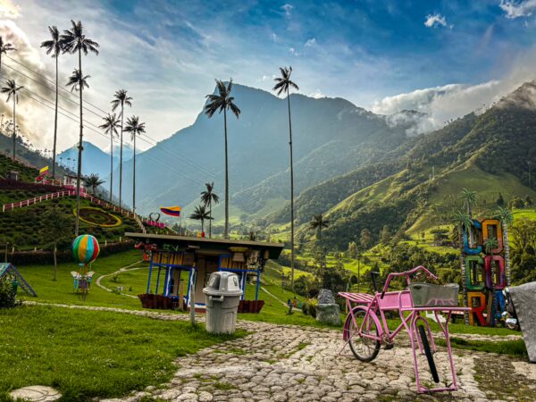 Vibrant Cocora Valley showcasing lush green hills, palm trees, and a pink bicycle near colorful playground equipment in Quindio, Colombia.