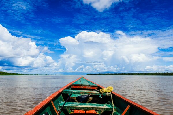 Bright blue skies with fluffy clouds reflect over the Amazon River, seen from the bow of a vibrant wooden boat in Santa Rosa, Peru.