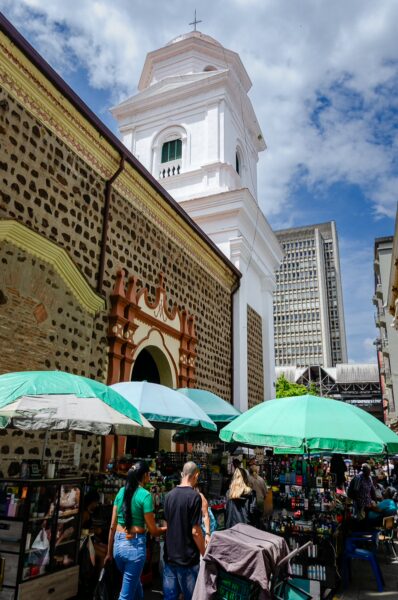 Nuestra Señora de la Candelaria in Medellín features a vibrant market scene with green umbrellas and a striking church tower.