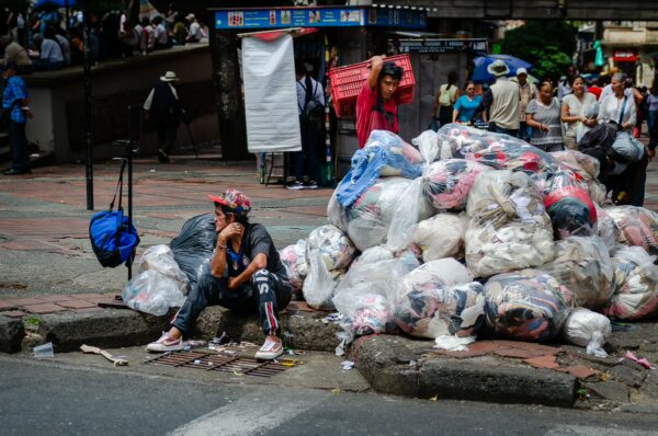 Street scene in central Medellín with a man beside large bags of clothing and pedestrians in the background