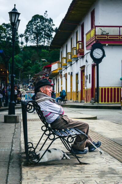A man resting on a bench in Plaza Bolívar, Salento, Quindío, Colombia, surrounded by colorful colonial buildings and greenery.