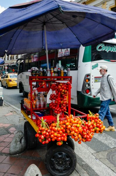 Vibrant fruit cart displaying ripe tomatoes and drinks under a blue umbrella in Medellín, showcasing local street vendor culture.