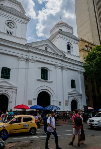 Basilica of Our Lady of Candelaria in central Medellín, with street vendors, taxis, and pedestrians outside