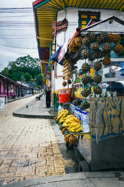 Vibrant market scene on Calle Real in Salento, Colombia, featuring a fruit stall laden with pineapples and bananas.
