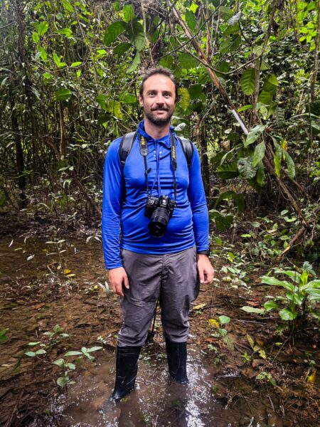 A man stands in the waterlogged Gamboa Nature Reserve in Loreto, Peru, surrounded by lush green foliage and tropical plants.