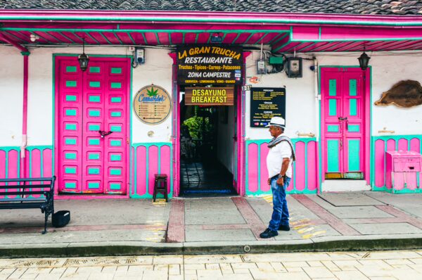 Brightly colored doors and a welcoming restaurant entrance line Calle Real in Salento, Quindío, showcasing vibrant Colombian architecture.