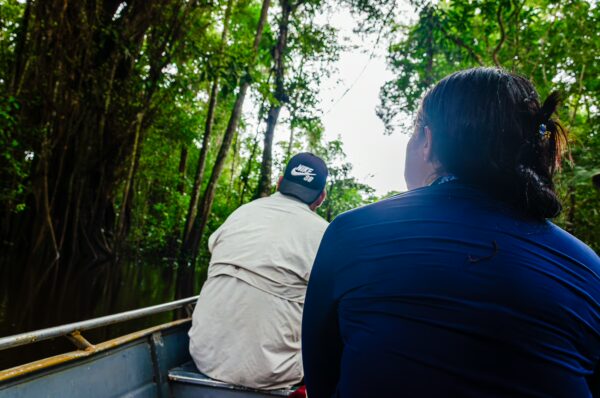 Two individuals sit in a boat navigating through the lush greenery of Gamboa Nature Reserve, Loreto, Peru.