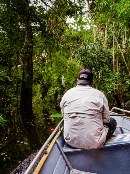 A man sits on a boat navigating through the lush greenery of Gamboa Nature Reserve in Loreto, Peru.