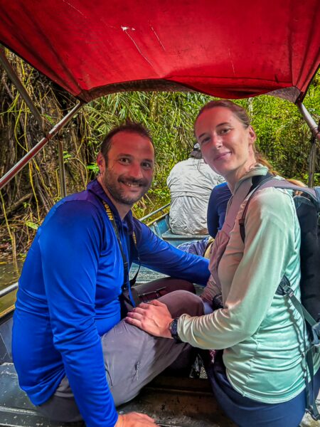 Couple enjoying a boat ride through lush greenery at Gamboa Nature Reserve, Loreto, Peru, with vibrant red canopy overhead.