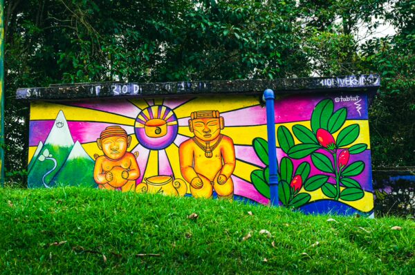 Vibrant mural featuring colorful figures and a sun emblem on a grassy hillside in Salento, Quindio, Colombia.