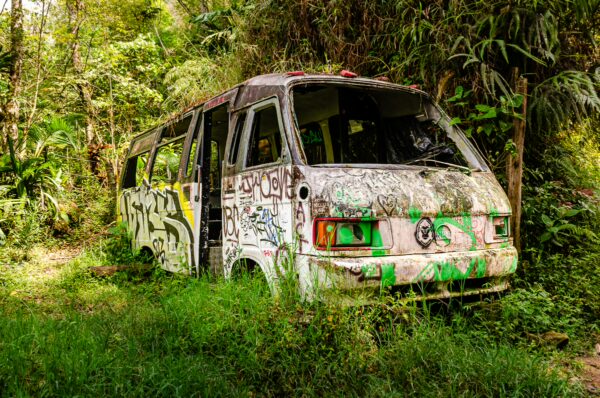 Colorful graffiti covers an abandoned bus, partially hidden by lush green vegetation near Santa Rita Waterfalls in Salento, Quindío, Colombia.