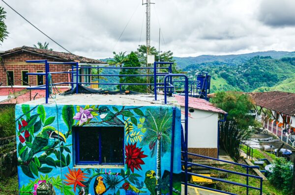 Colorful mural featuring tropical plants and birds on a building with a scenic view of the mountains in Salento, Quindio, Colombia.