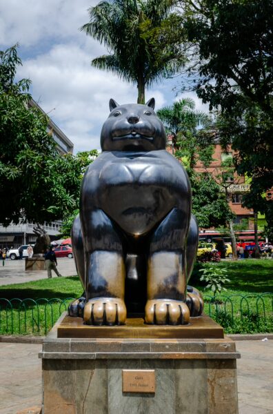 Bold sculpture of a cat in Plaza Botero, surrounded by vibrant greenery and palm trees in Medellín, Antioquia.