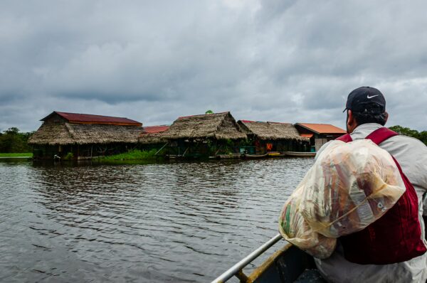 A man with a bag watches traditional thatched-roof homes along Pirana Lake in Gamboa Nature Reserve, Loreto, Peru.