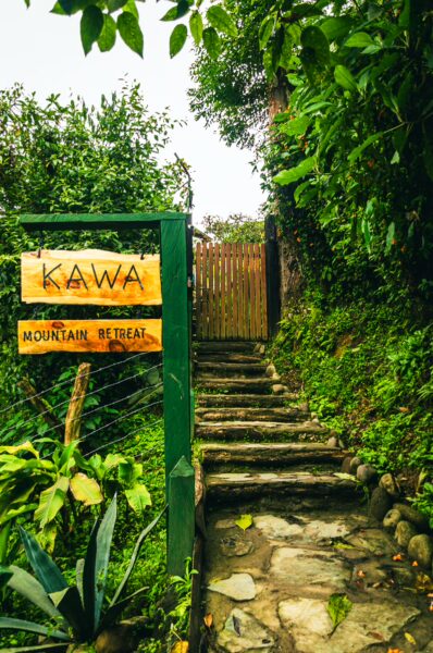 Kawa Mountain Retreat entrance with a wooden sign and stone steps, surrounded by lush greenery in Salento, Quindio, Colombia.