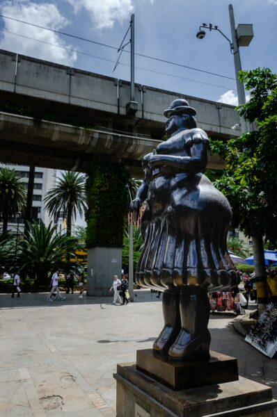 A large Botero sculpture stands in Plaza Botero, surrounded by palm trees and lively street activity in Medellín, Colombia.