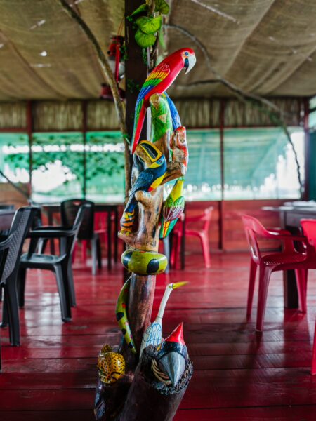 Colorful carvings of macaws and wildlife adorn a wooden post inside a vibrant restaurant at Pirana Lake, Gamboa Nature Reserve, Loreto, Peru.