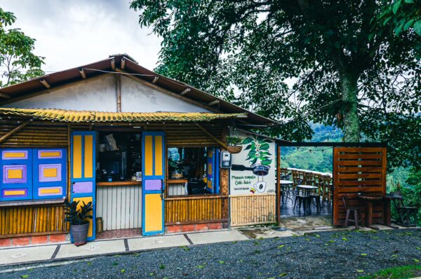 Colorful wooden café with vibrant doors and a lush green backdrop in Salento, Quindío, Colombia, invites visitors to relax.