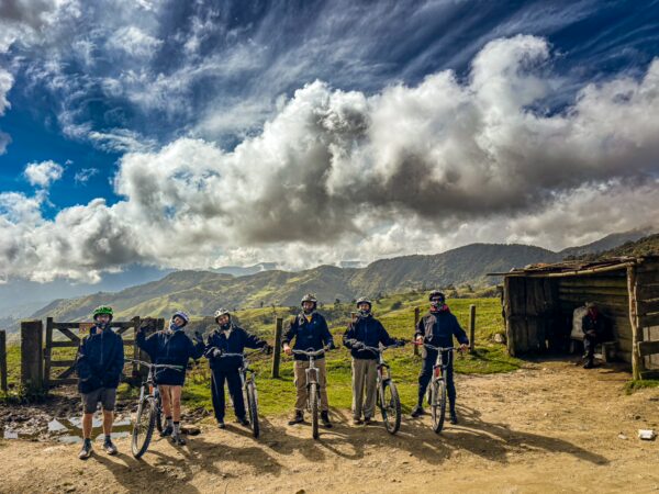 Bikers pause against a backdrop of rolling hills and dramatic clouds in Carbonera Valley, Quindío, Colombia.