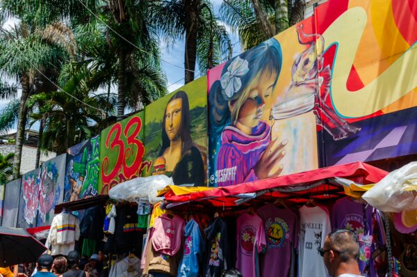 Vibrant street art adorns the market stalls in Comuna 13, Medellín, with colorful murals and a variety of clothing.