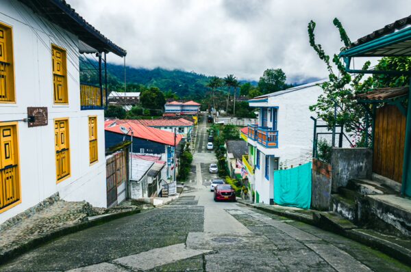 Colorful houses with yellow doors line the steep street in Salento, Quindio, Colombia, framed by lush green mountains.